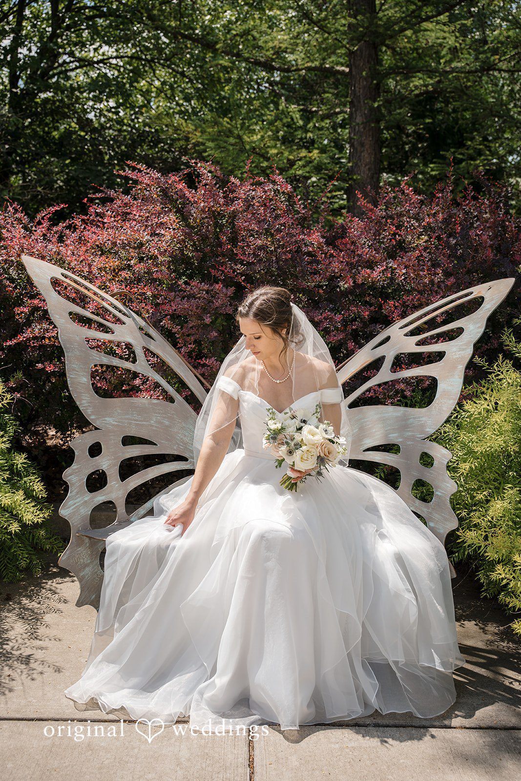 Emily + Maxwell A bride sitting on a white bench styled to look like large butterfly wings.