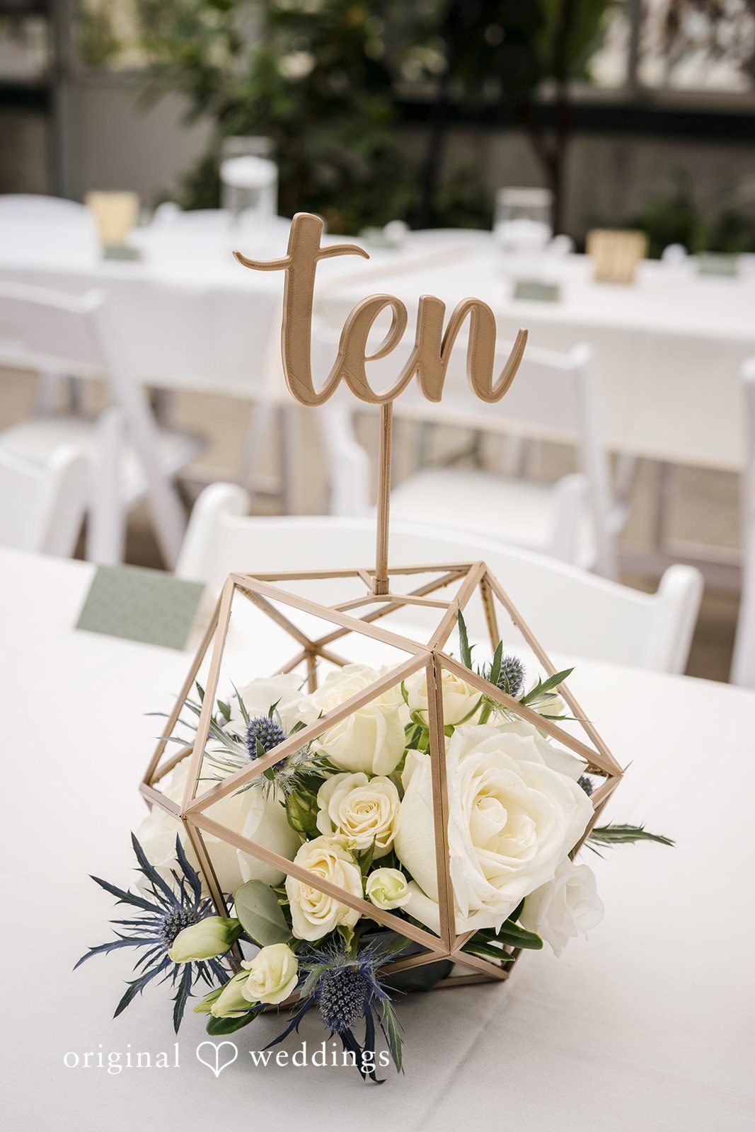 Emily + Maxwell A close-up of a geometric glass terrarium centerpiece displaying the table number ten.