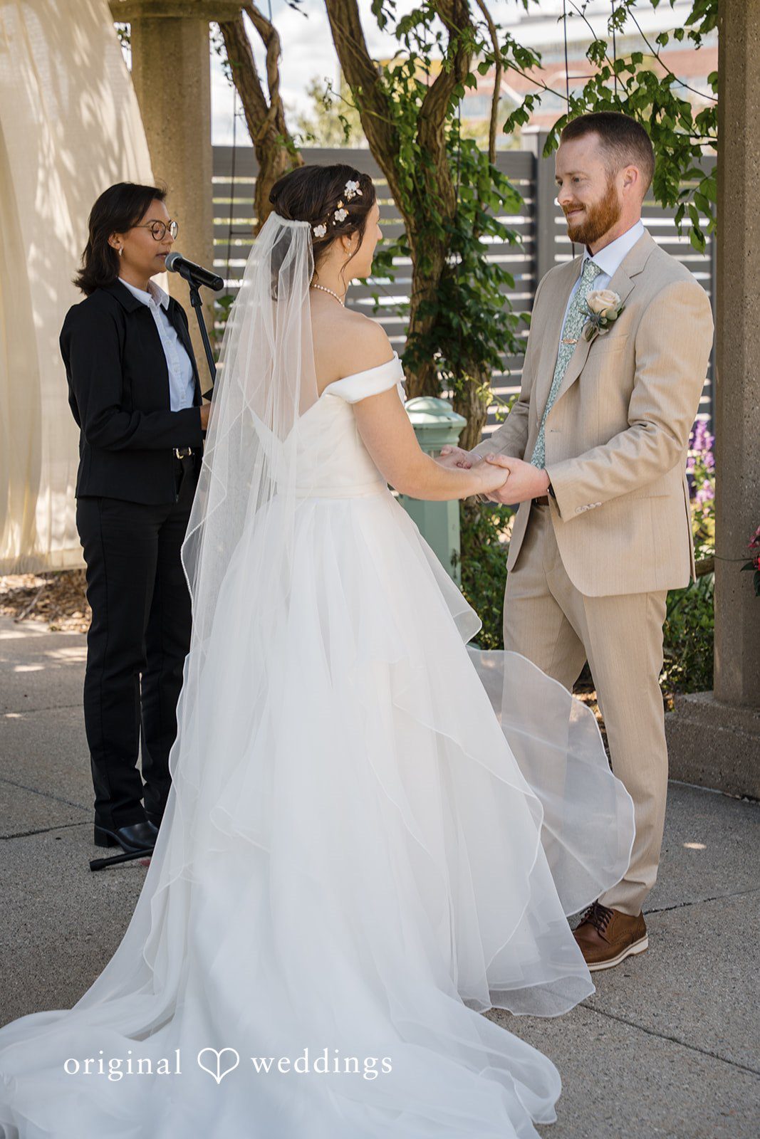 Emily + Maxwell A bride and groom holding hands and facing each other during their wedding ceremony.