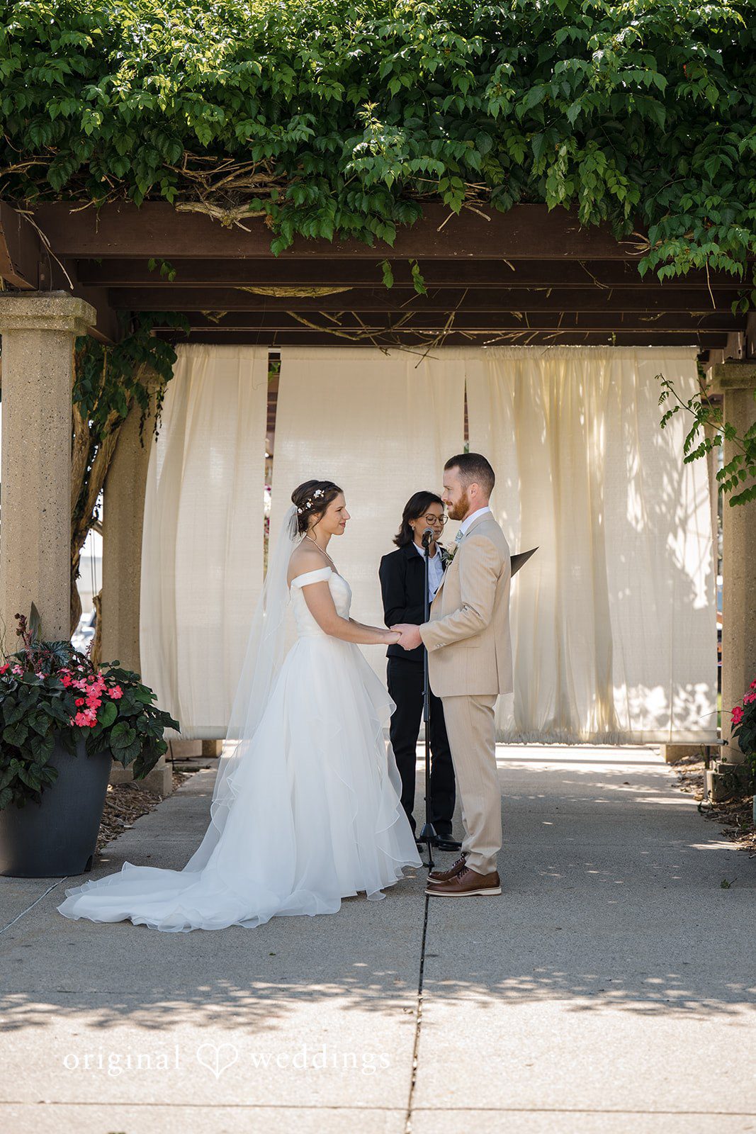 Emily + Maxwell A bride and groom standing together under a decorated wooden pergola structure.
