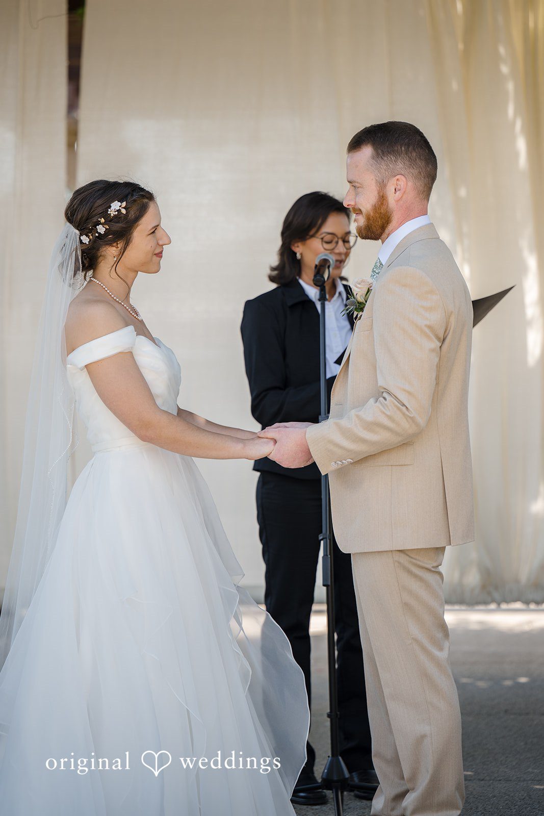 Emily + Maxwell A bride and groom holding hands while standing before an officiant during a ceremony.