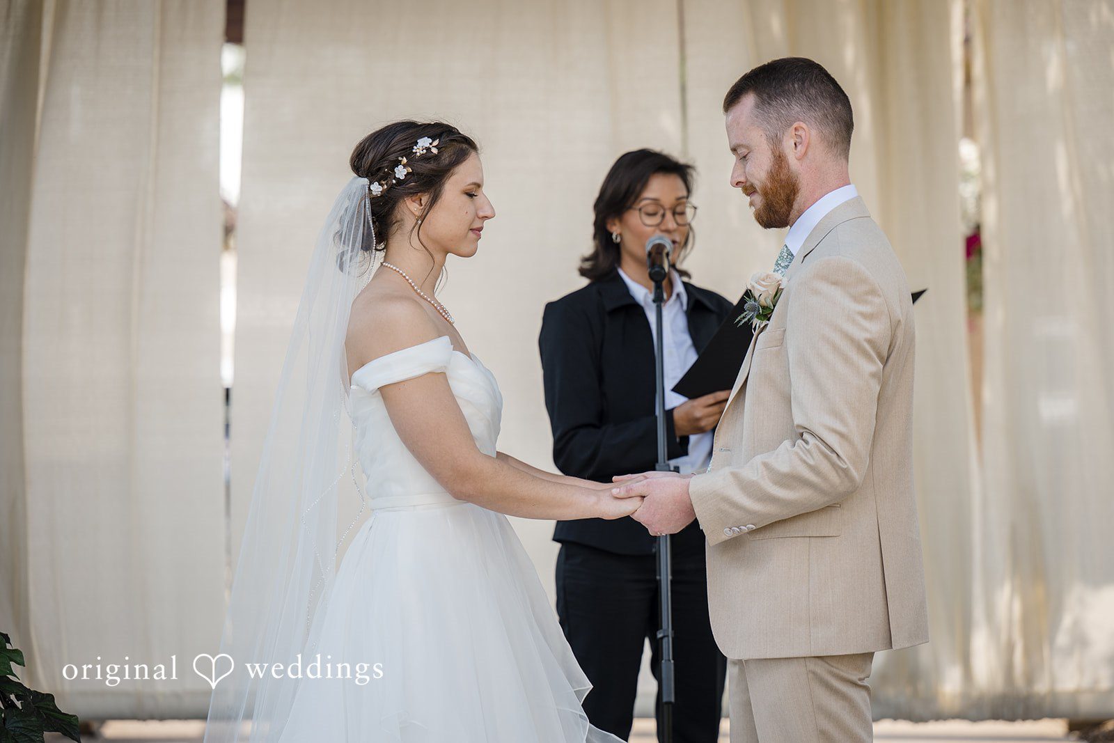 Emily + Maxwell A bride and groom facing each other while standing before an officiant during their ceremony.