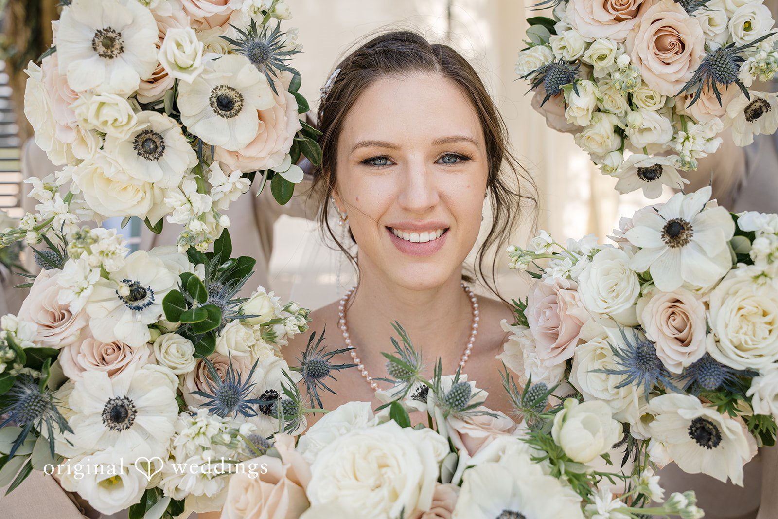 Emily + Maxwell A close-up portrait of a smiling bride standing in front of a lush floral wall.
