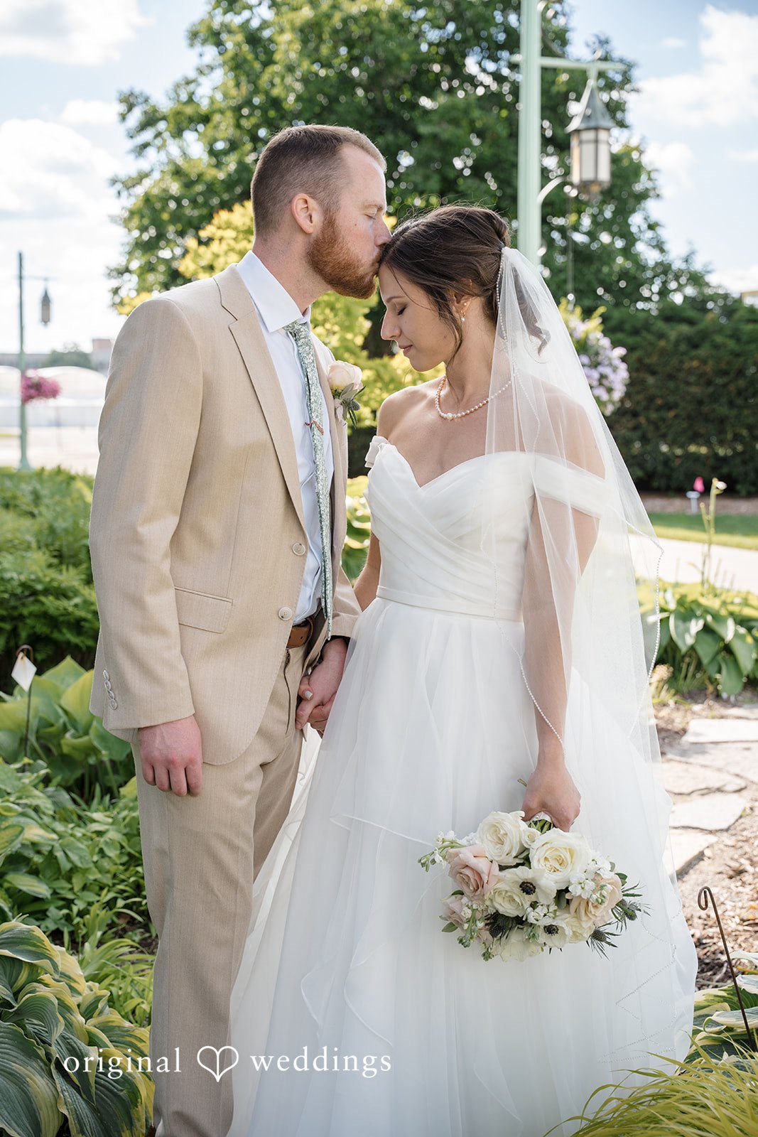 Emily + Maxwell A bride and groom holding hands and walking together along an arched green bridge.