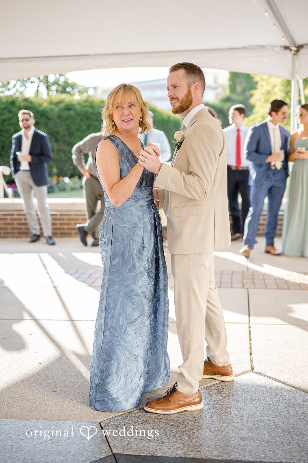 Emily + Maxwell A man in a tan suit dancing with a woman in a blue dress during a wedding reception.