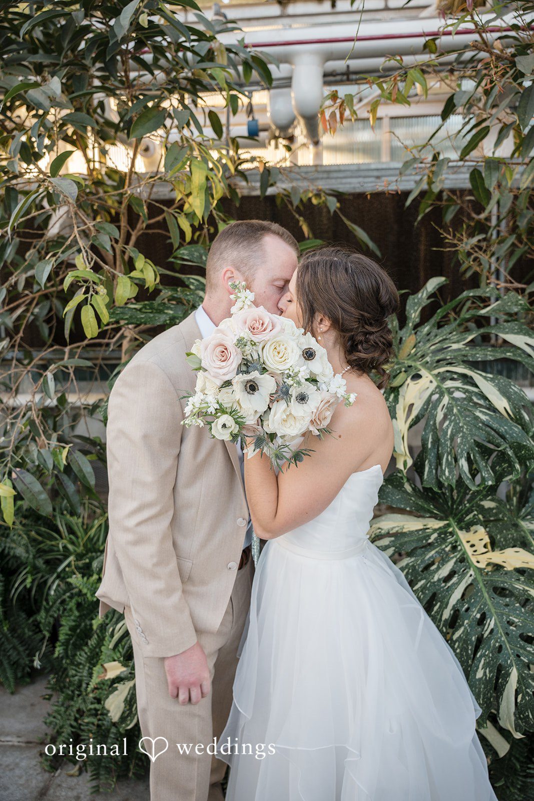 Emily + Maxwell A groom holding a white bouquet while kissing his bride on the forehead.