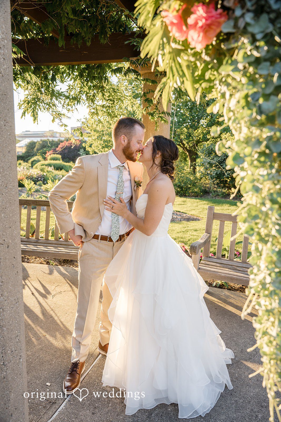 Emily + Maxwell A bride and groom leaning in for a kiss along a sunlit pathway.