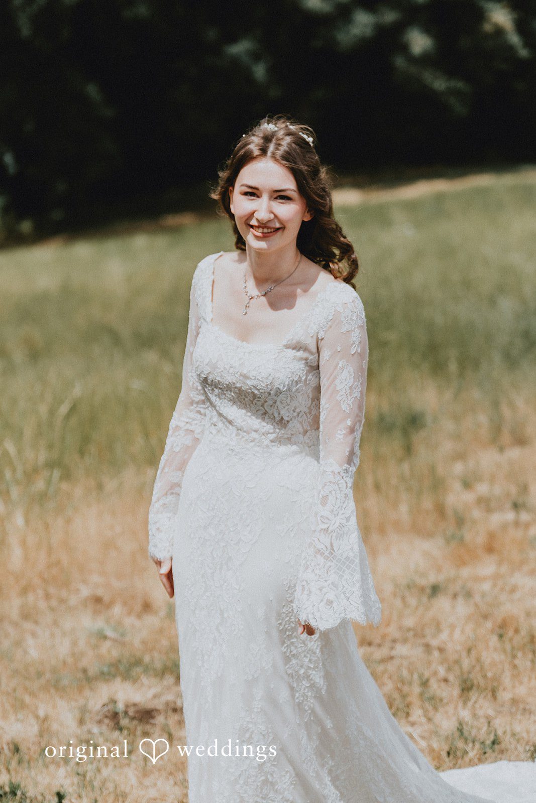 Catherine + Gabriel Bride in a long lace wedding gown standing in a grassy field.