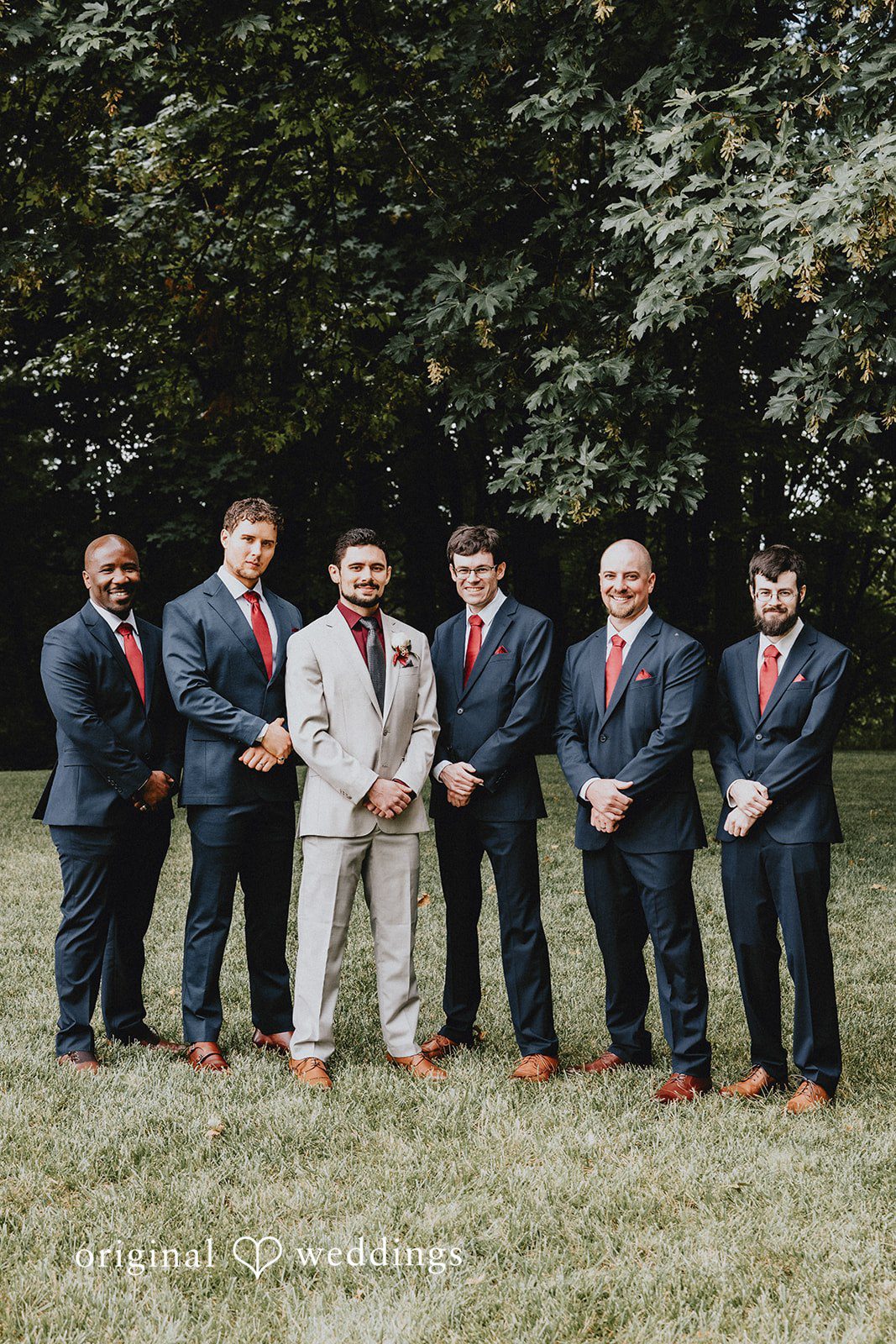 Catherine + Gabriel Groom and groomsmen posing together in matching light-colored suits in a park.