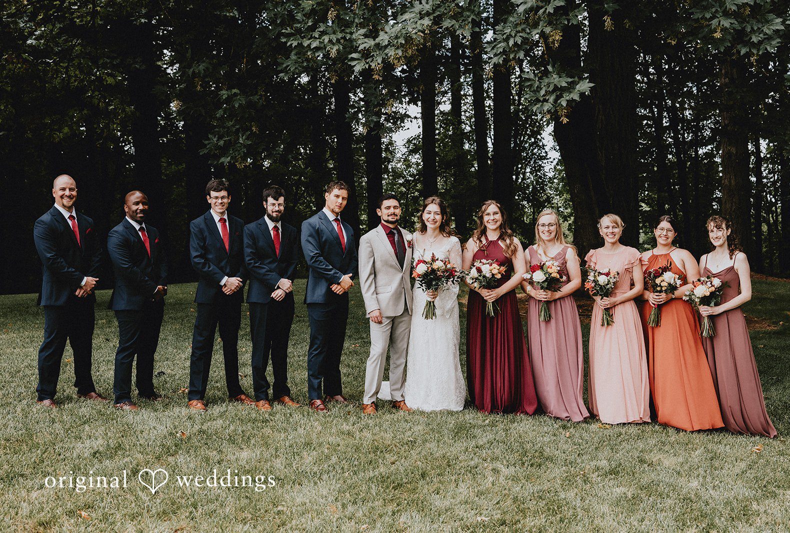 Wedding party consisting of bridesmaids and groomsmen posing in a line among trees captured by Portland Wedding Photographers from Original Weddings.