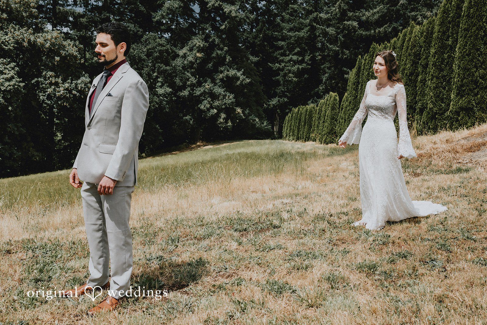 Catherine + Gabriel Bride and groom standing far apart on a grassy hillside facing one another.