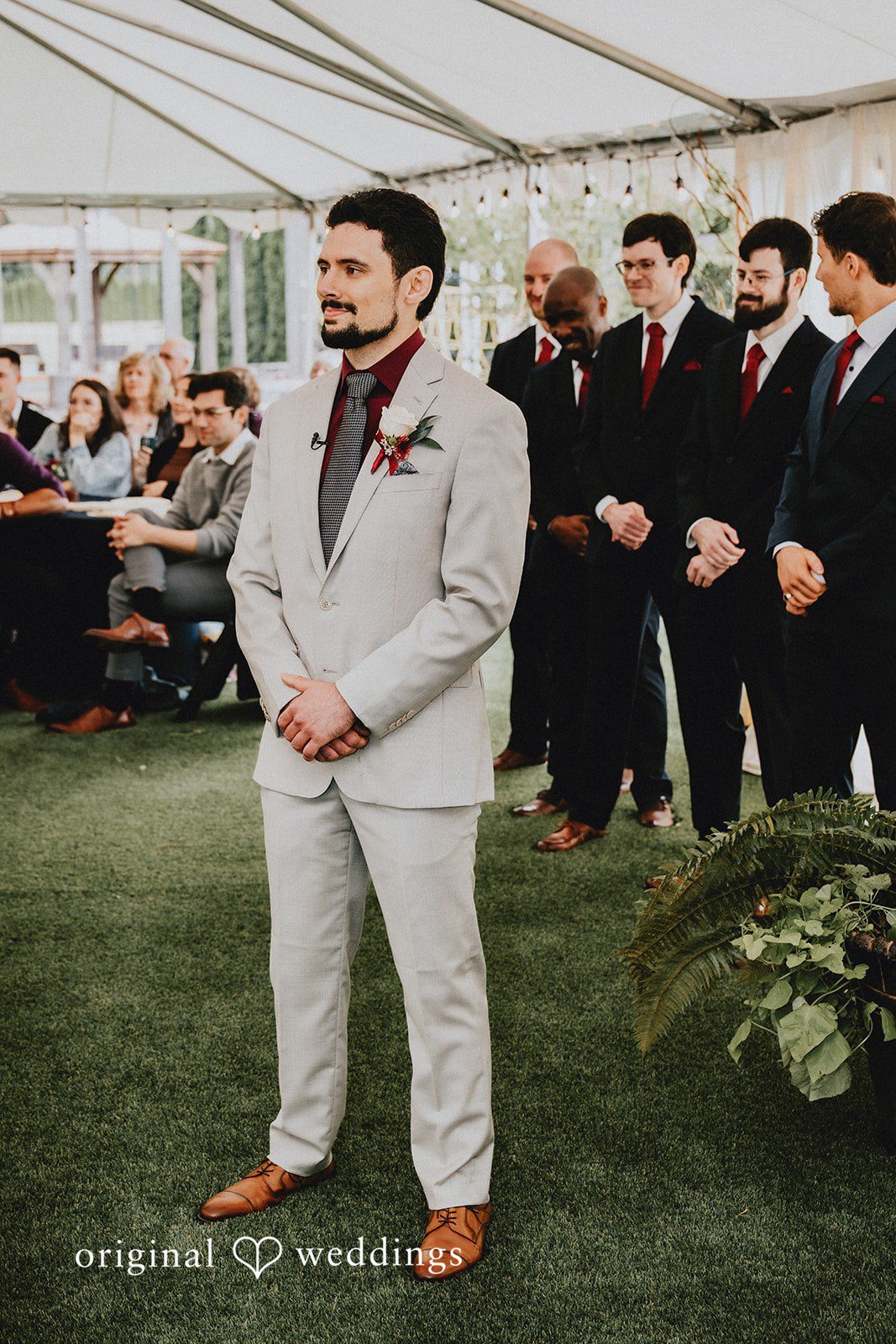 Catherine + Gabriel Groom in a light beige suit smiling ahead during a ceremony.
