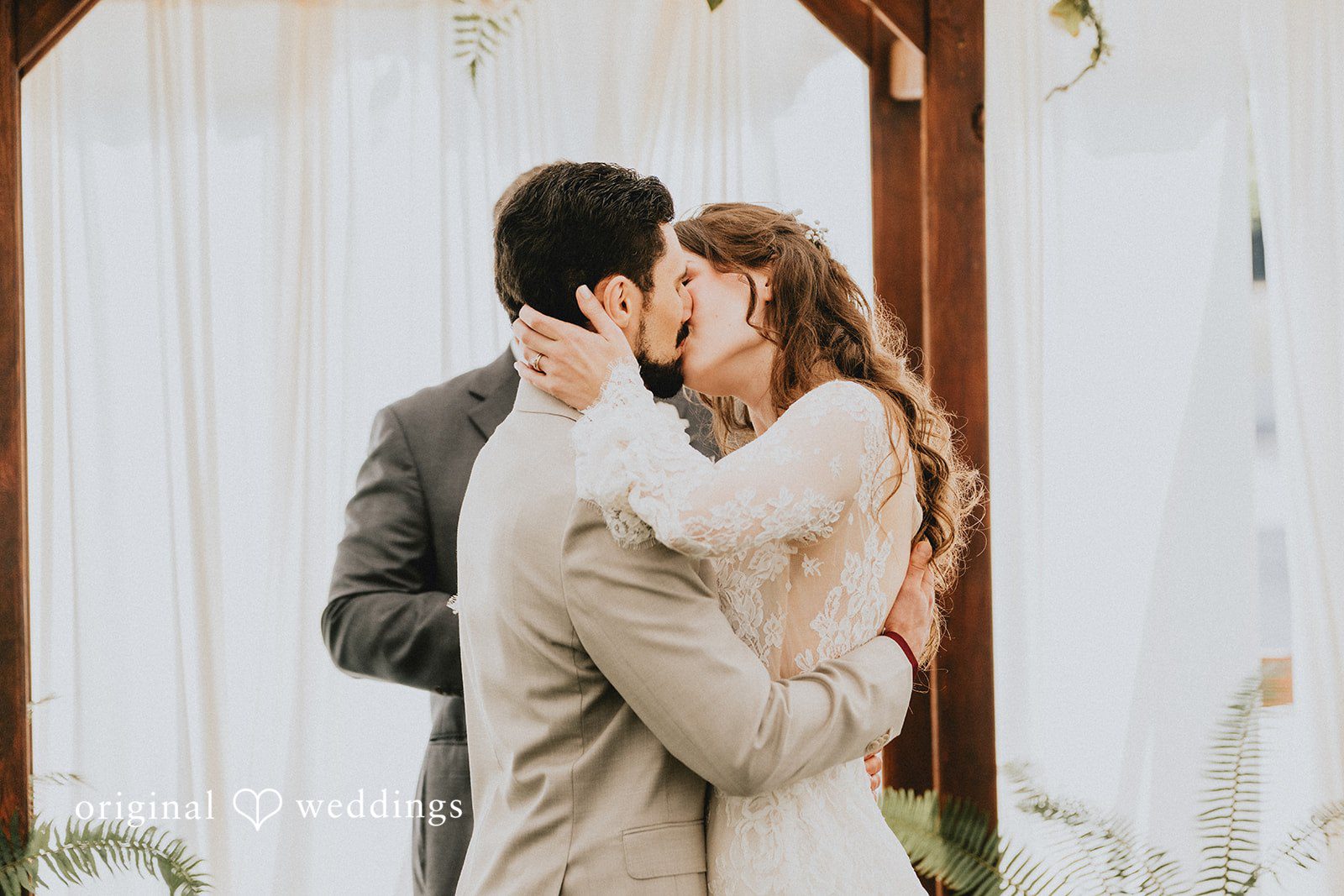 Catherine + Gabriel Bride and groom sharing an intimate embrace and kissing against a white fabric backdrop.