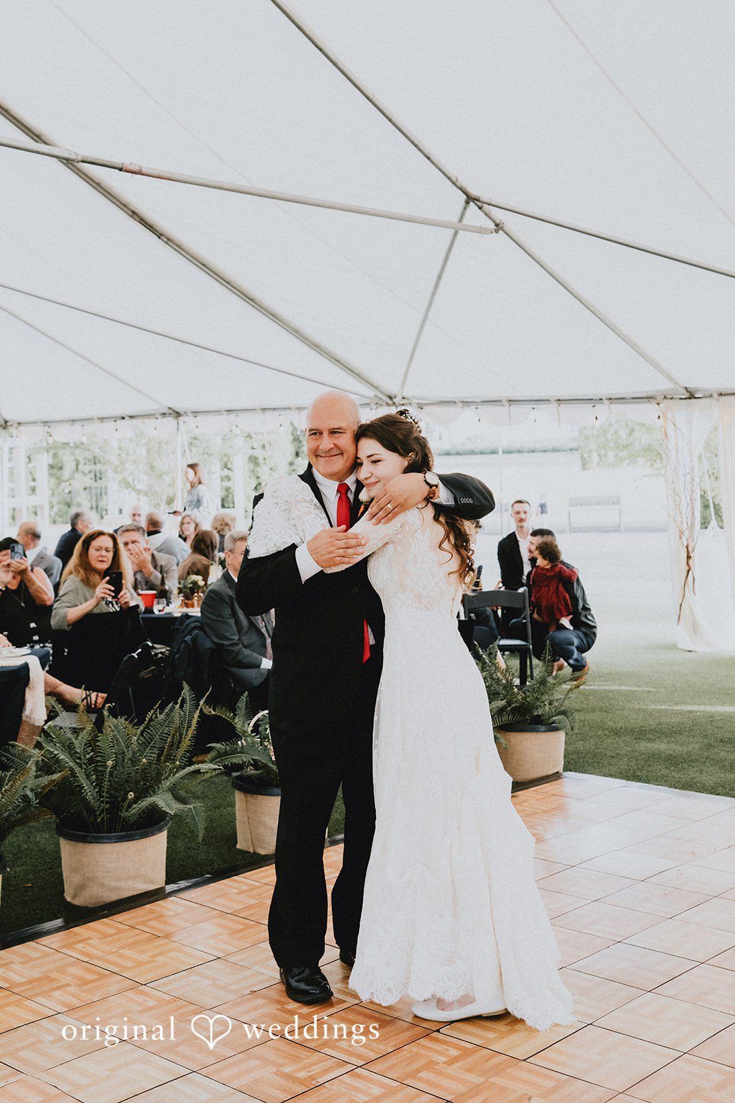 Catherine + Gabriel Bride in a white gown hugging a man in a black suit while dancing under a tent.