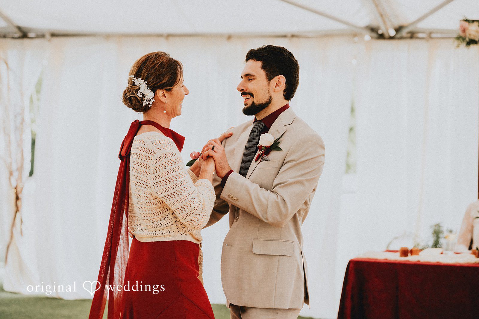 Catherine + Gabriel Groom in a beige suit smiling while dancing with a woman in a red and cream outfit.