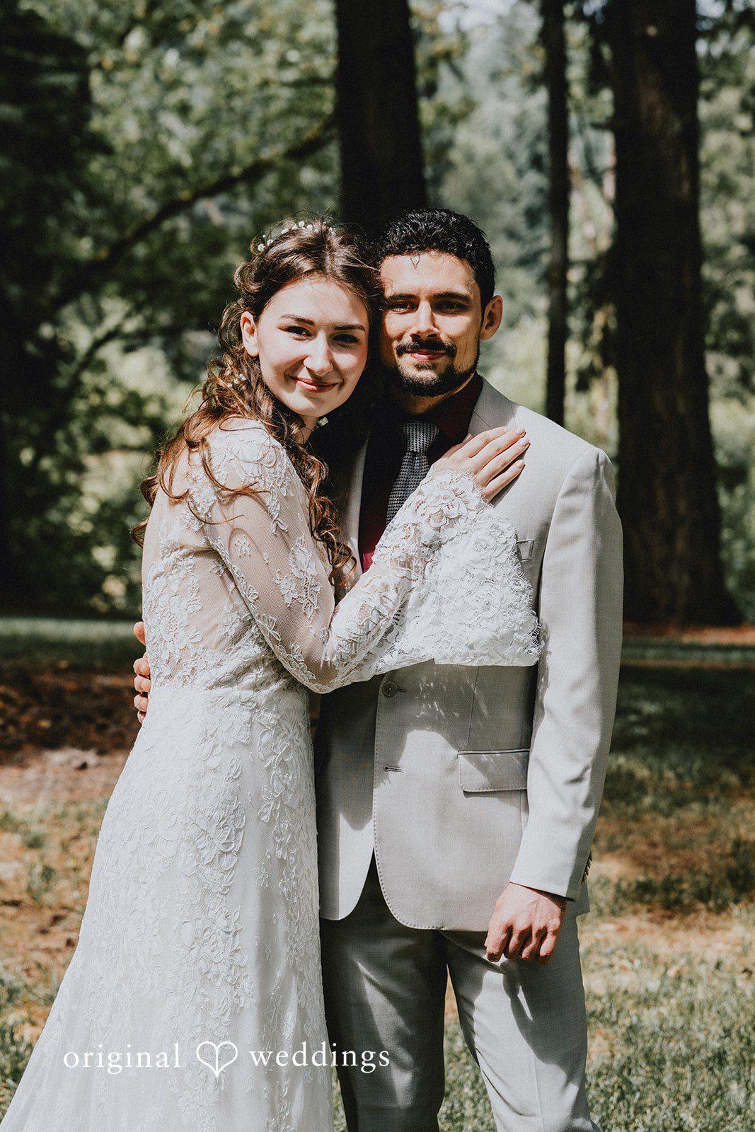 Catherine + Gabriel Bride and groom posing together while standing among tall pine trees.