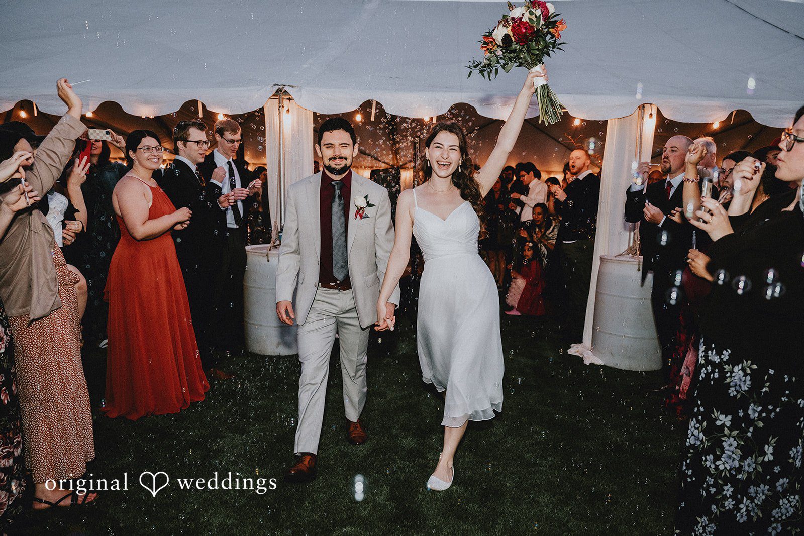 Catherine + Gabriel Newlyweds walking together through a crowd of wedding guests under a reception tent.