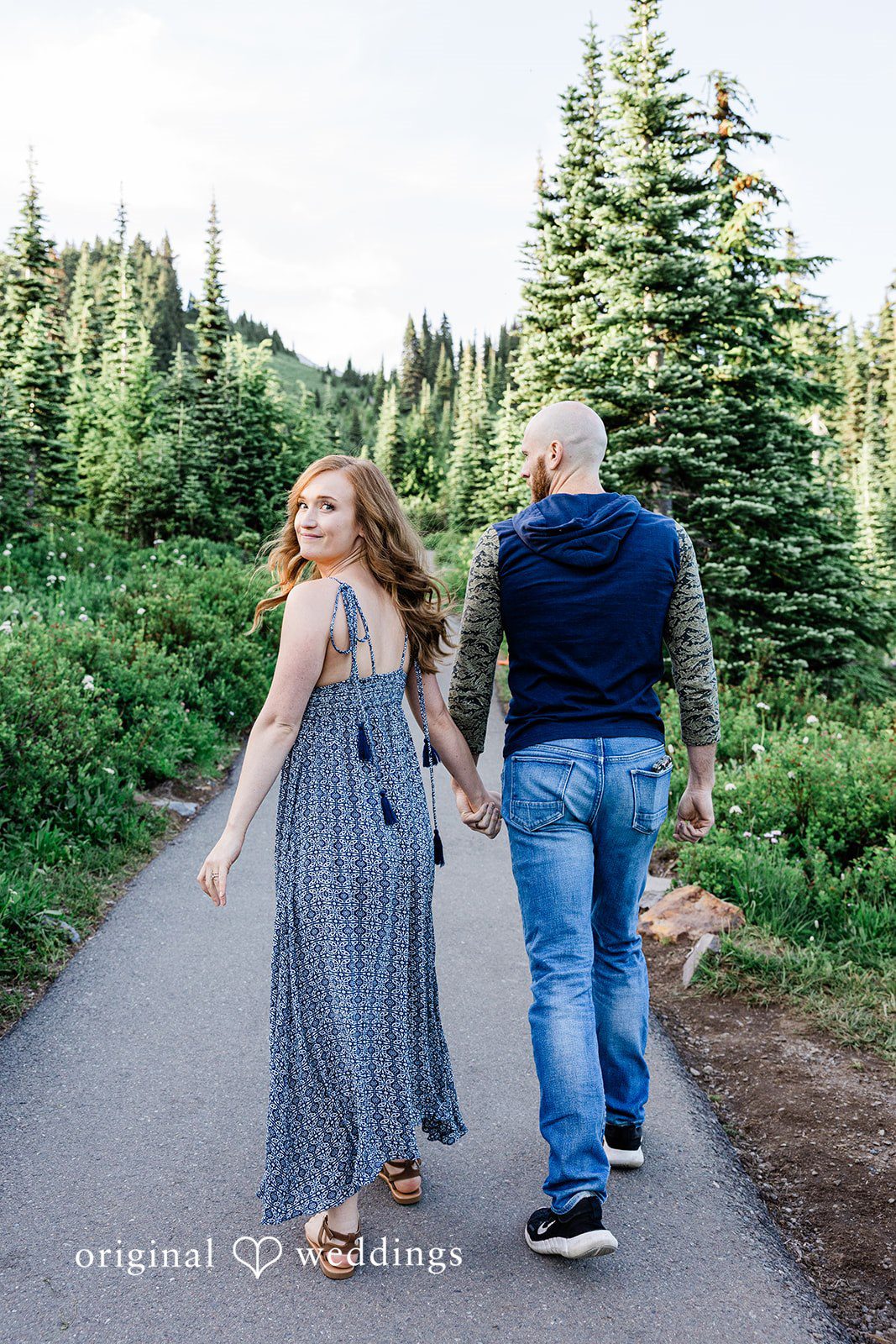 Megan + Kevin A man and a woman hold hands while walking away into a lush green forest path.