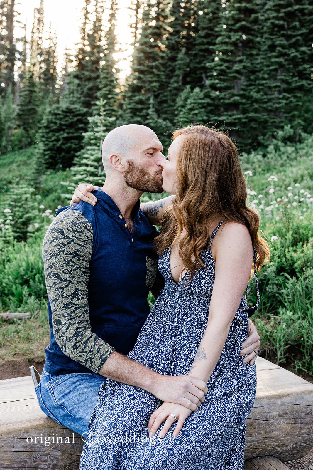 Megan + Kevin A man kisses a smiling woman while sitting on a rustic wooden path.