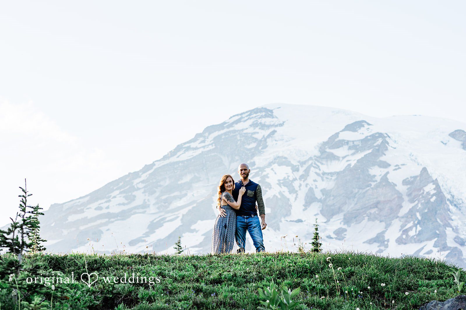 Megan + Kevin A small silhouette of a man and a woman standing in front of a massive snowy mountain peak.