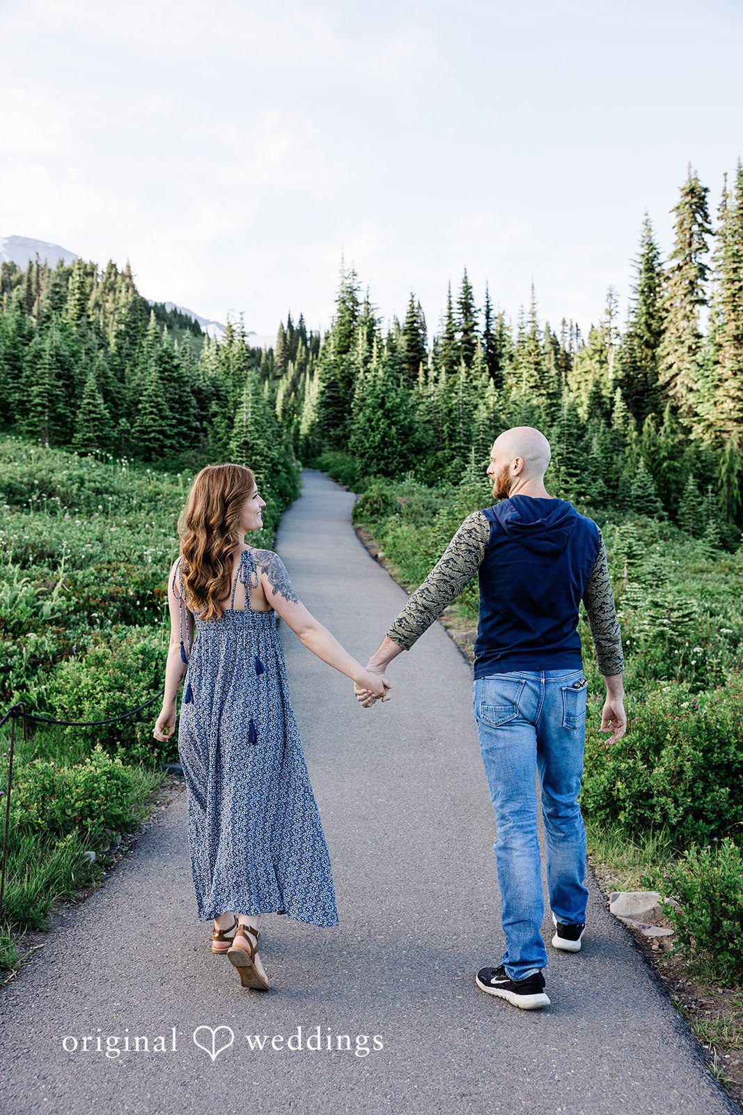 Megan + Kevin A man and a woman hold hands while walking away down a tree-lined asphalt road.