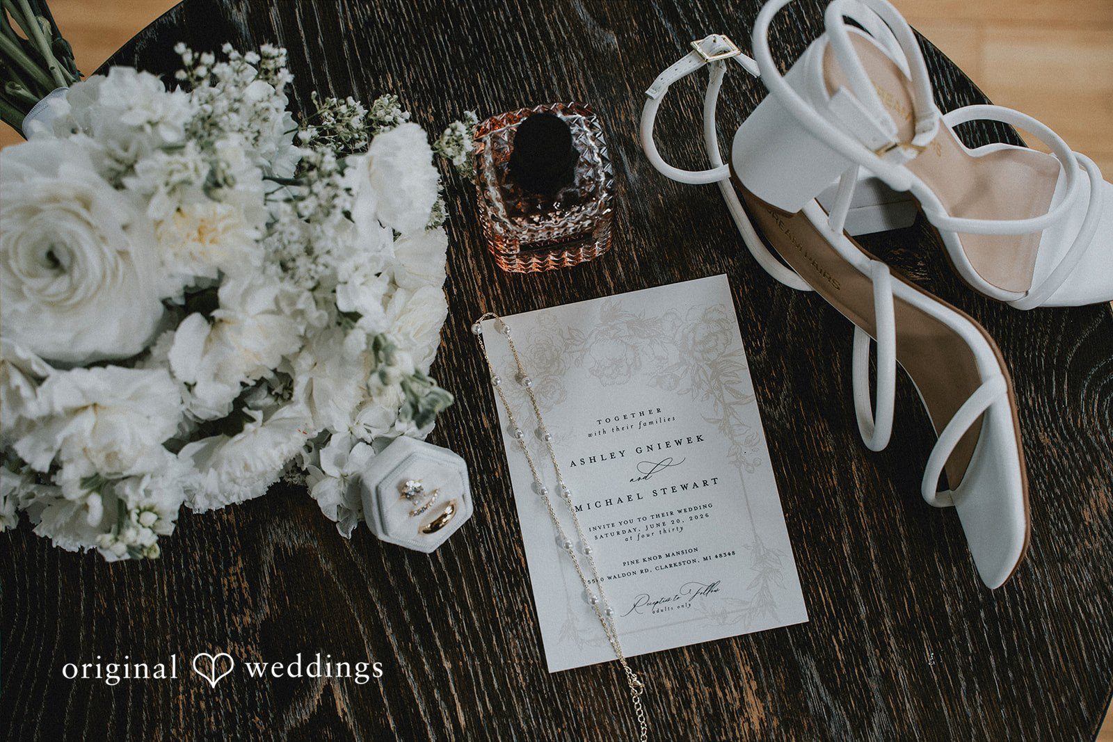 Flat lay of bridal shoes, invitations, and white flowers.