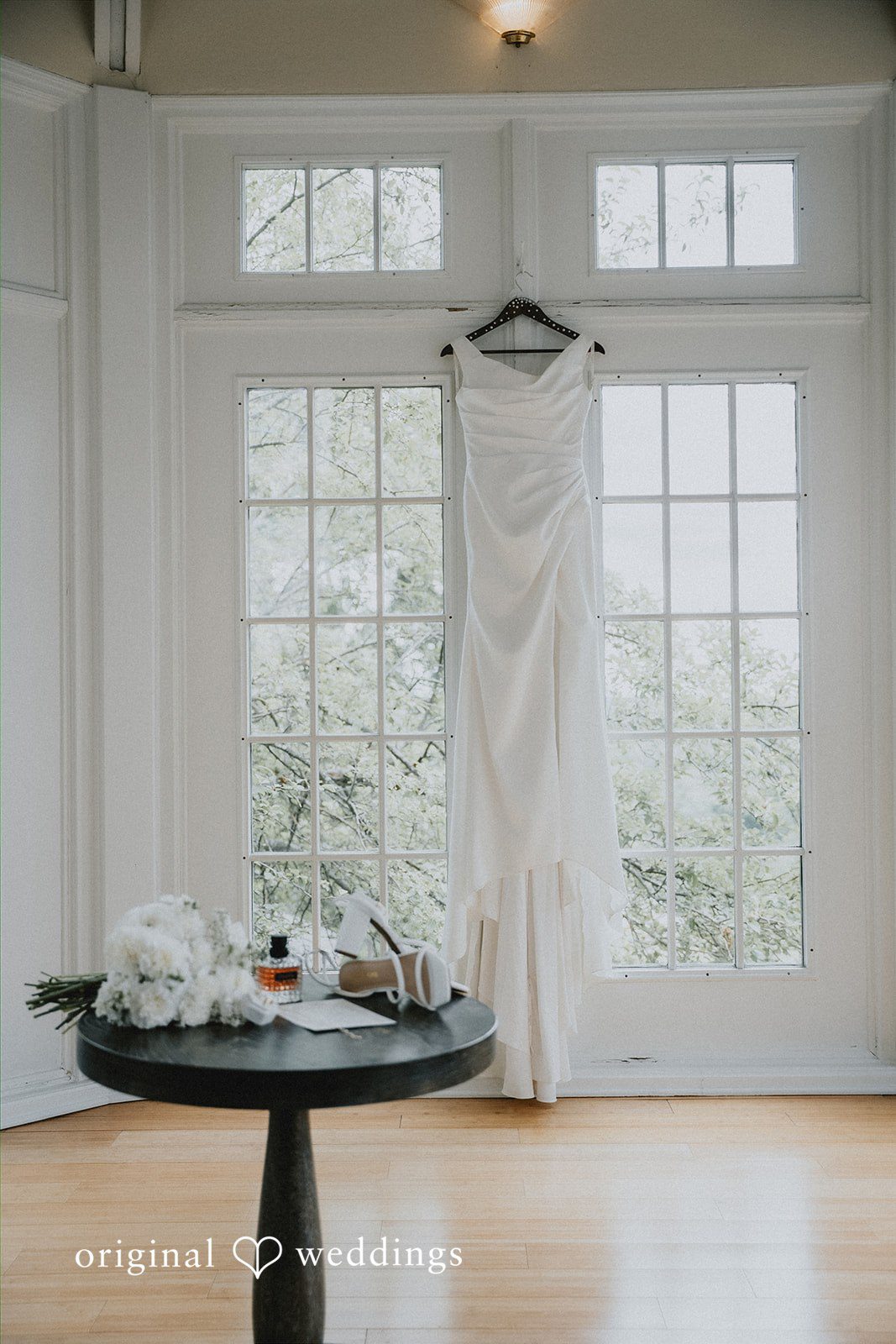 Wedding dress hanging in front of large windows.