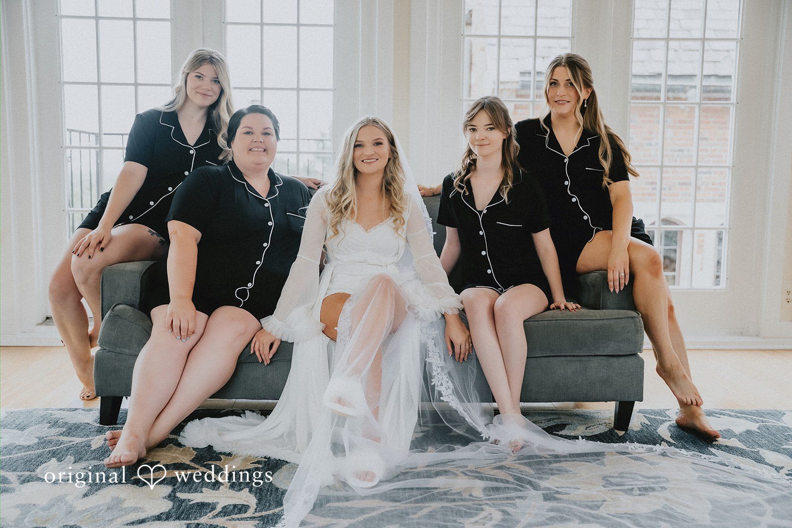 Bride sitting on a couch surrounded by bridesmaids.