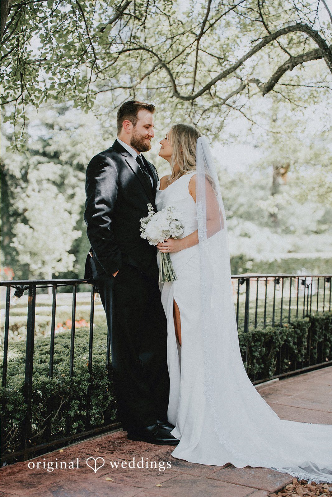 Bride and groom holding hands beneath leafy tree branches.