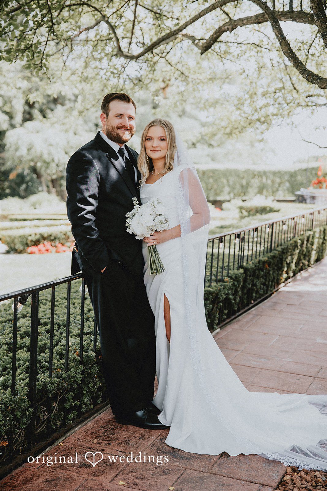 Bride and groom posing together along a stone brick walkway.