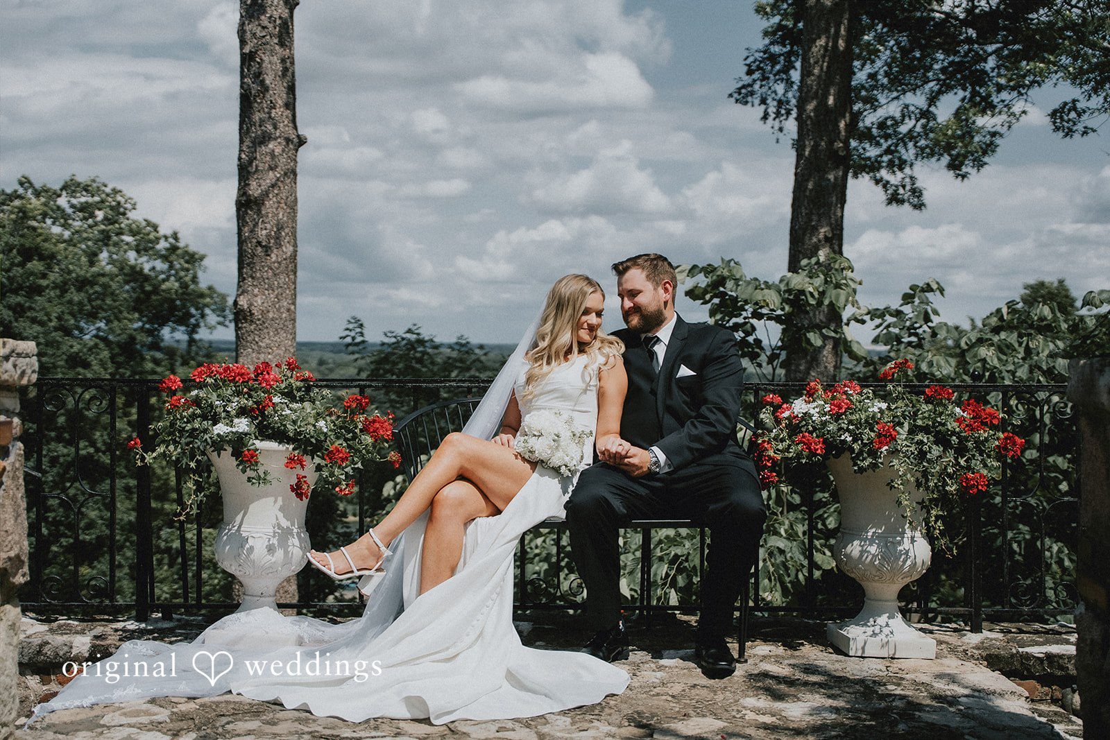 Bride sitting on groom's lap amidst a rustic forest backdrop.