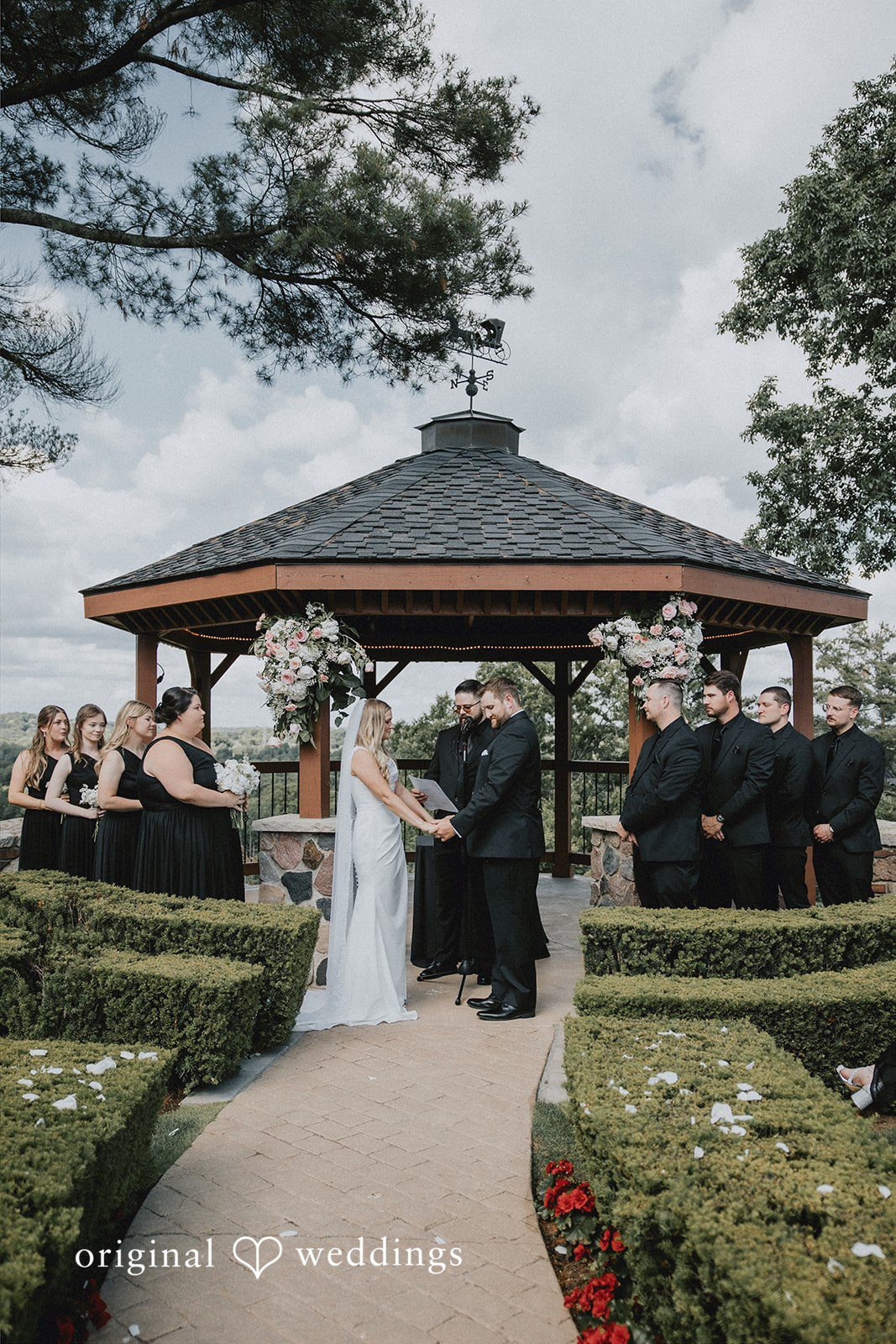 Wedding ceremony taking place under a wooden garden gazebo.