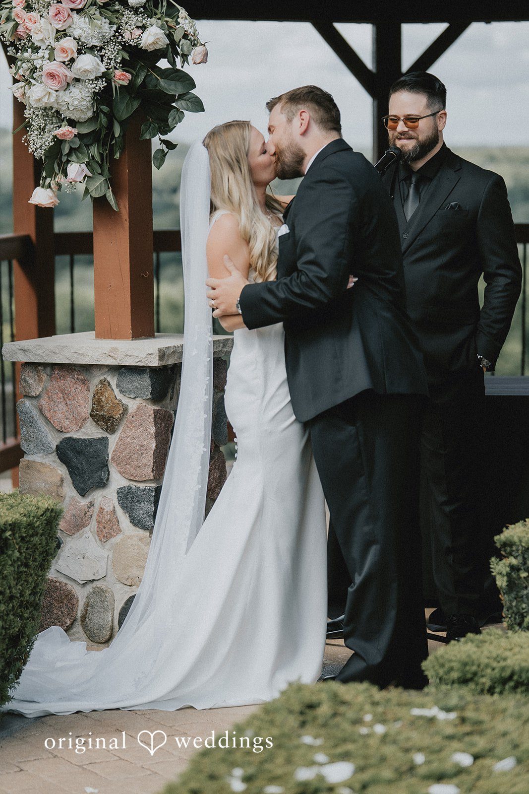 Bride and groom embracing near a stone wall structure.