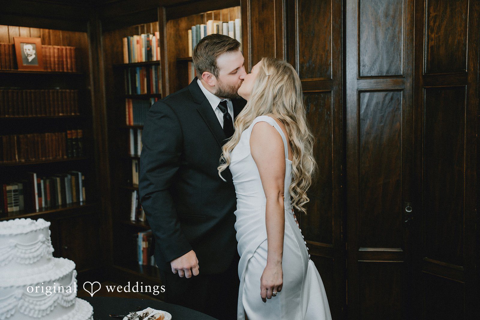 Bride and groom kissing in front of dark wood paneling.