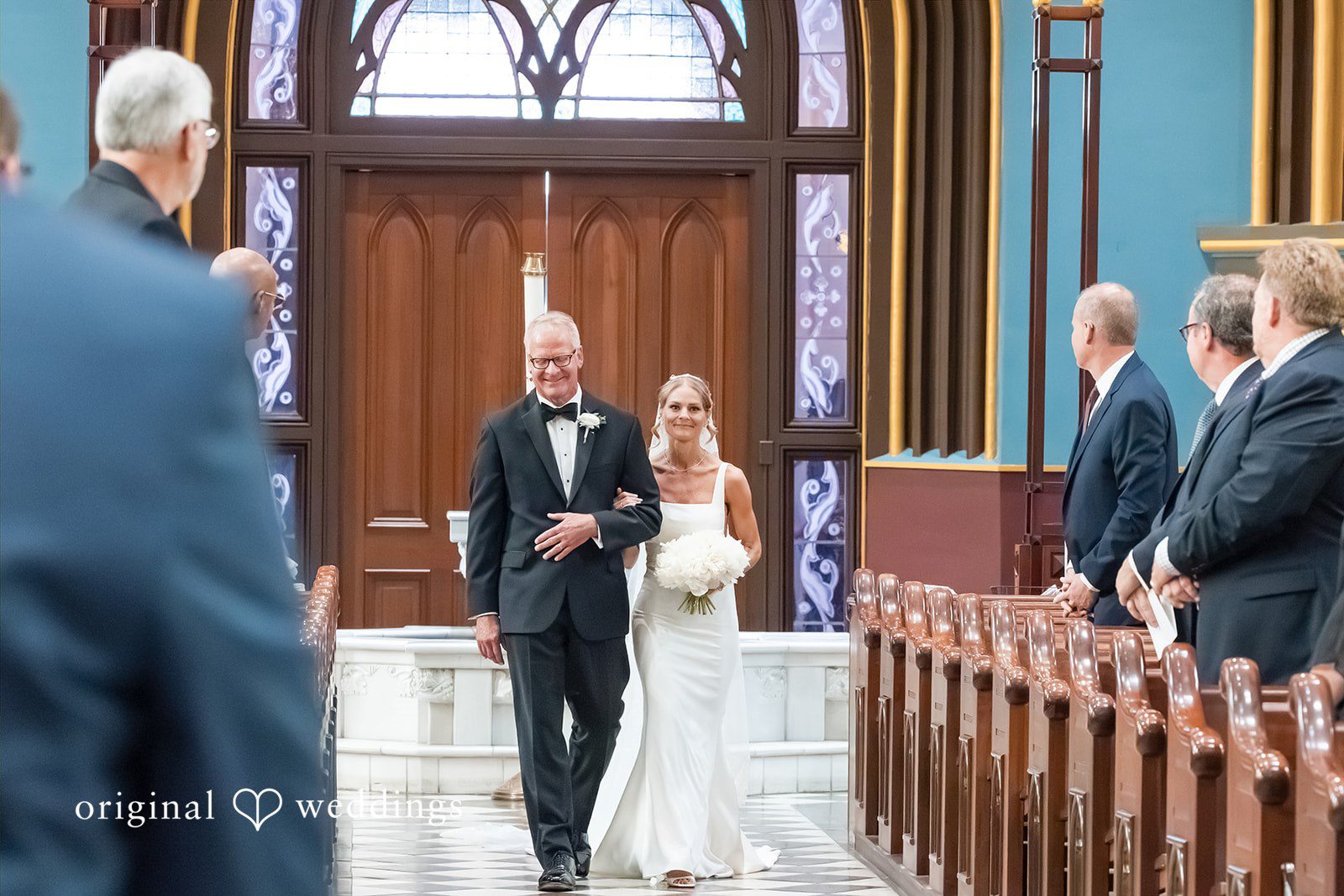 Bride and man walking down the aisle while wedding guests applaud.