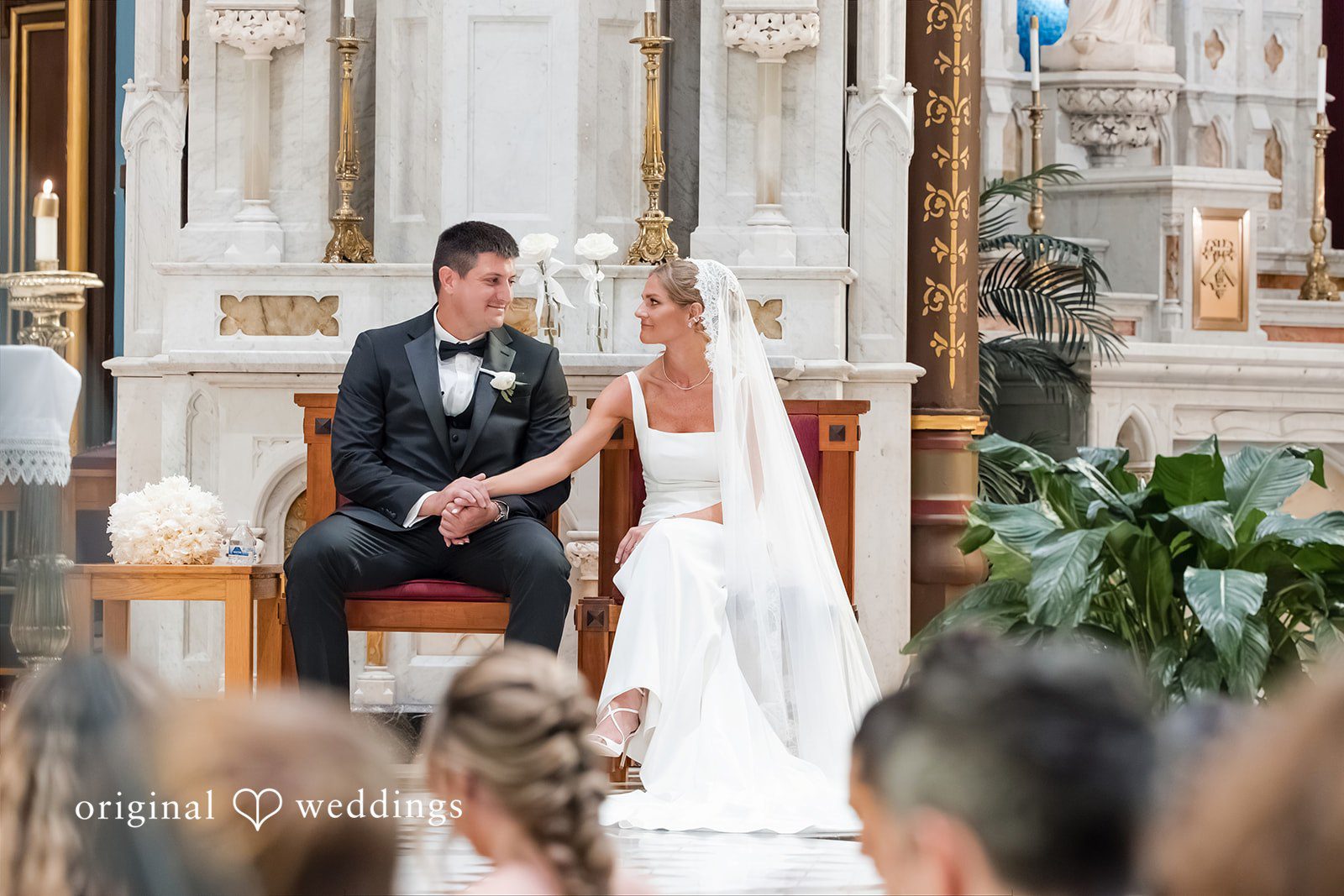 Bride and groom holding hands and sitting together at church.