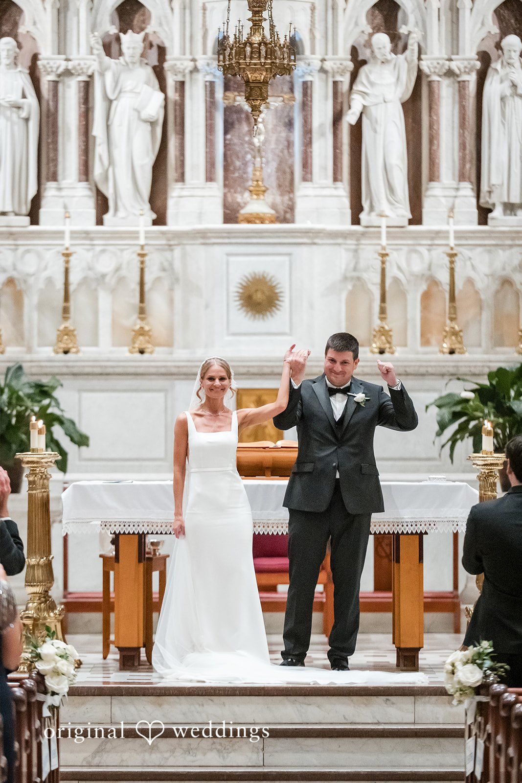 Bride and groom holding hands and smiling at the front of a church altar.