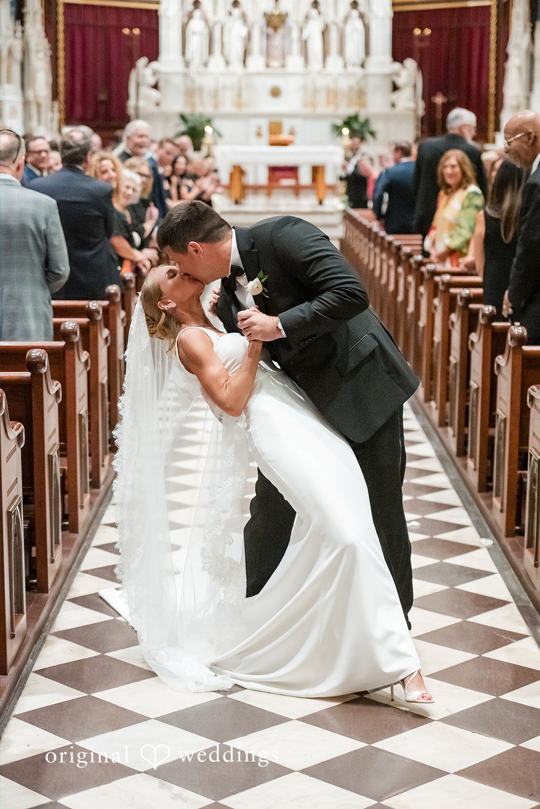 Groom dipping and kissing the bride in the middle of a church aisle.