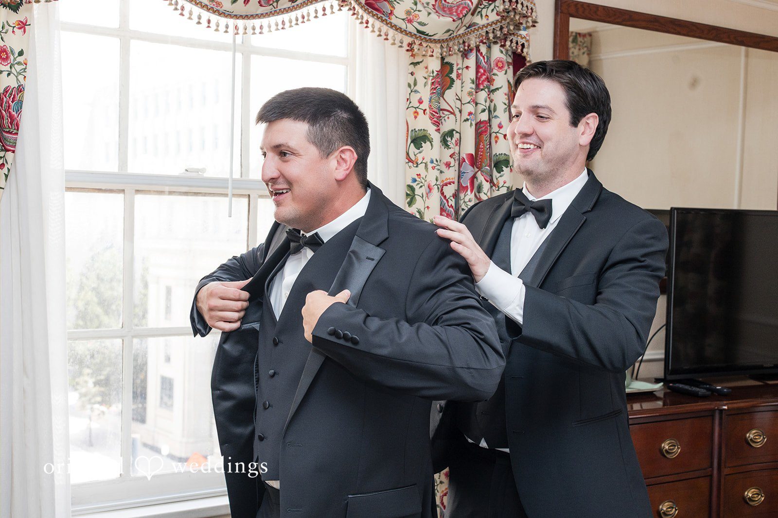 Groom adjusting his jacket while talking to another man in a tuxedo.