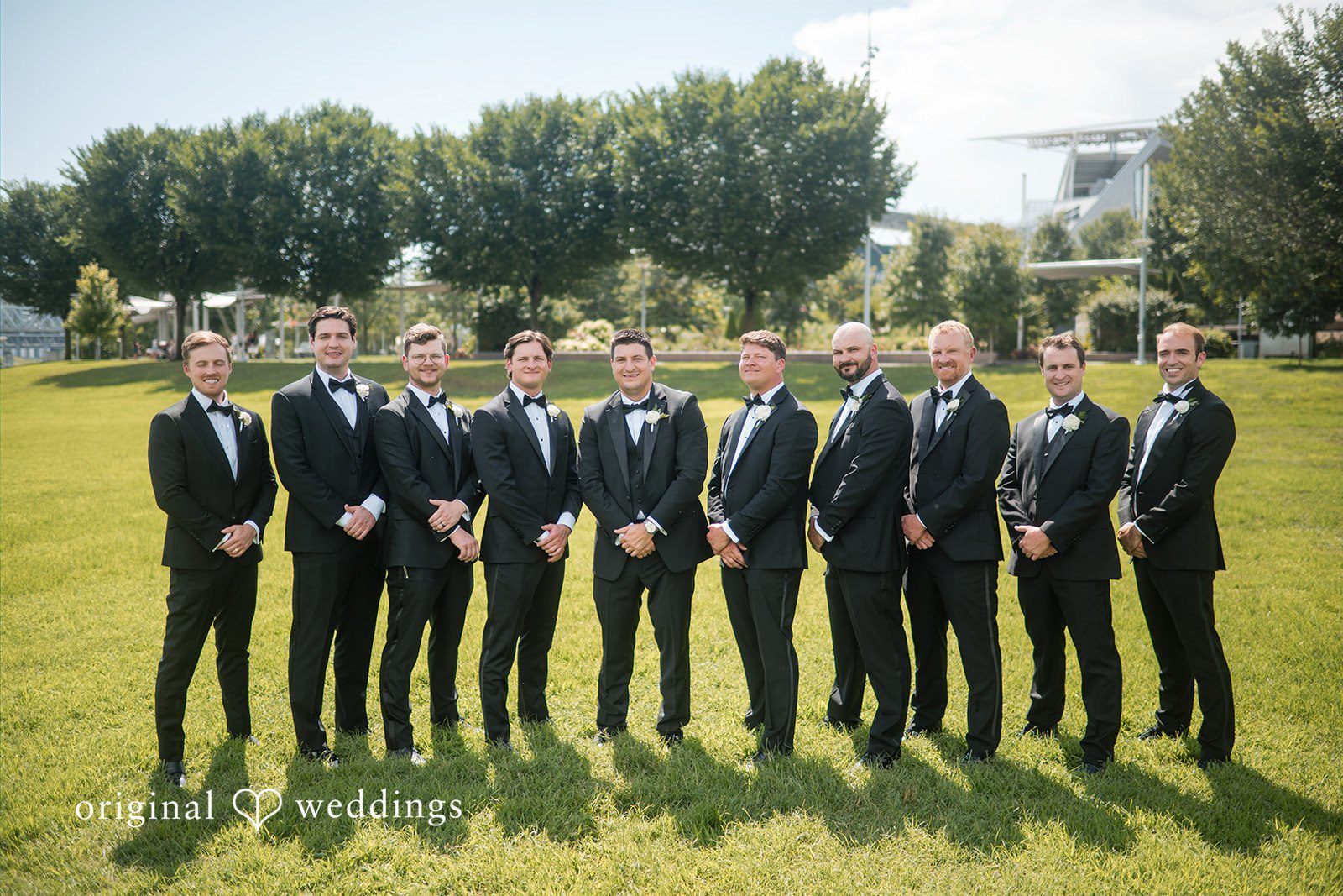 Groom and groomsmen standing in a long line on a lawn.