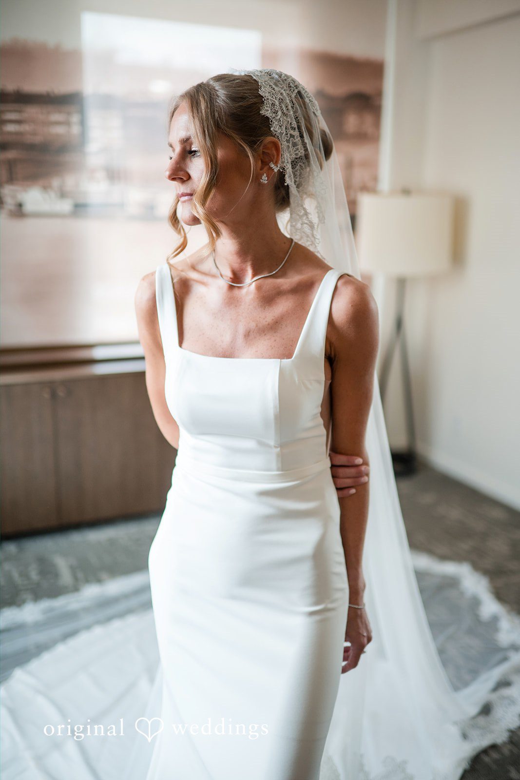Bride in a white wedding gown posing next to a window.