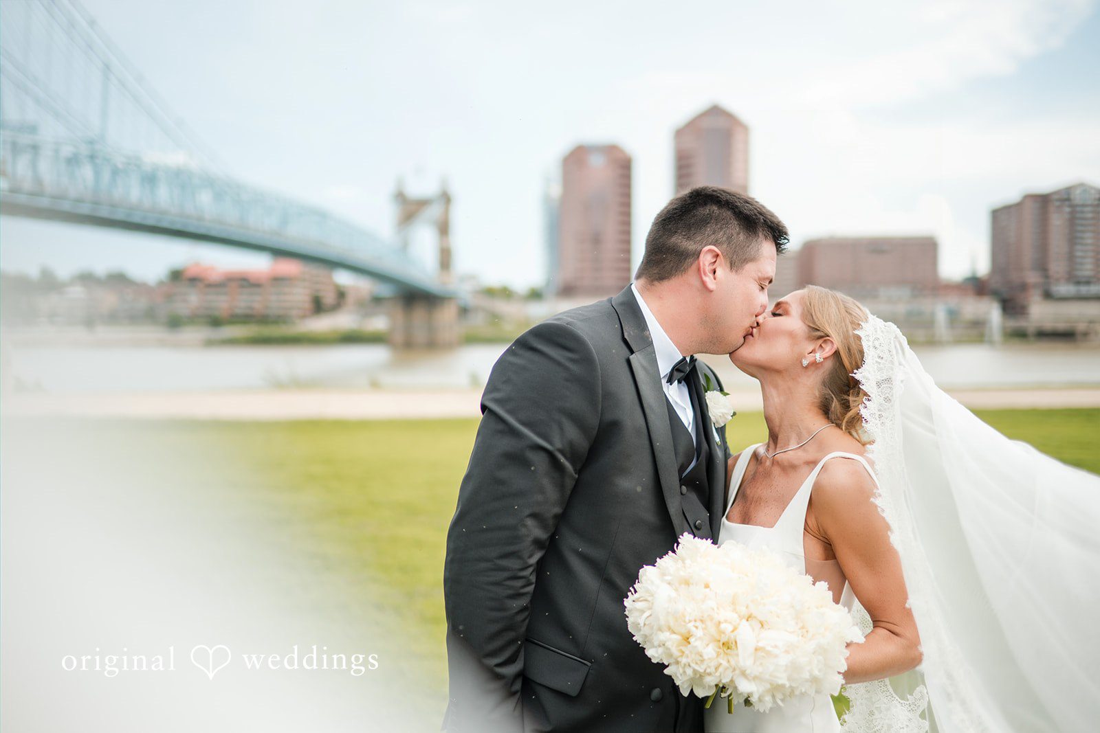 Bride and groom kissing with a large suspension bridge in the background.