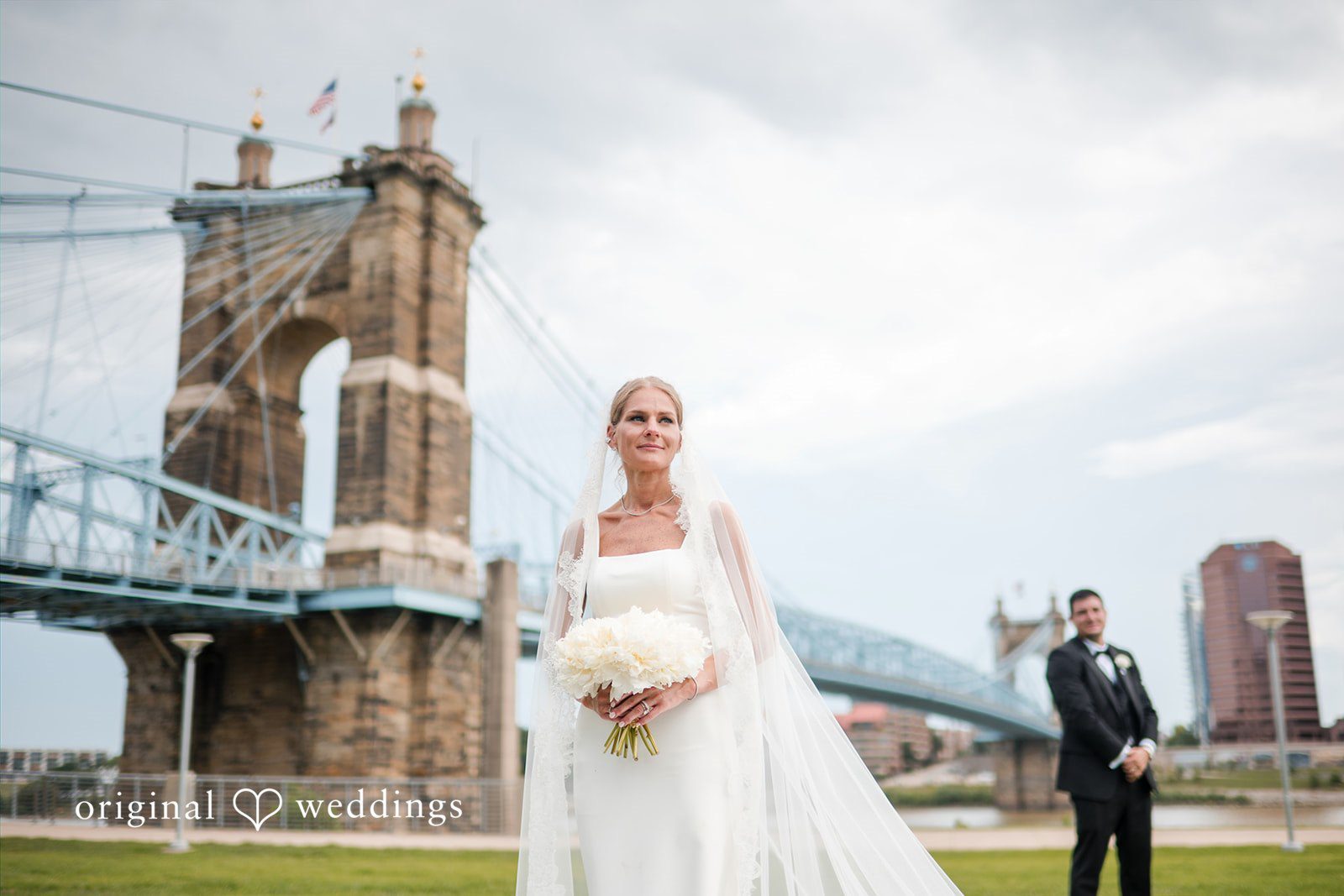 Bride holding her bouquet and smiling with a large bridge in the background.