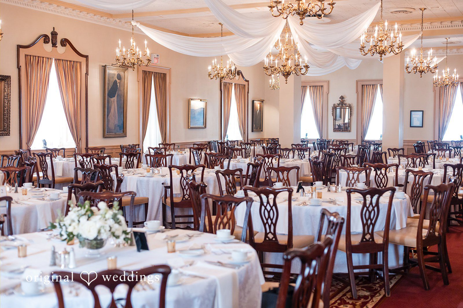 Empty reception hall filled with formally decorated dining tables and chairs.