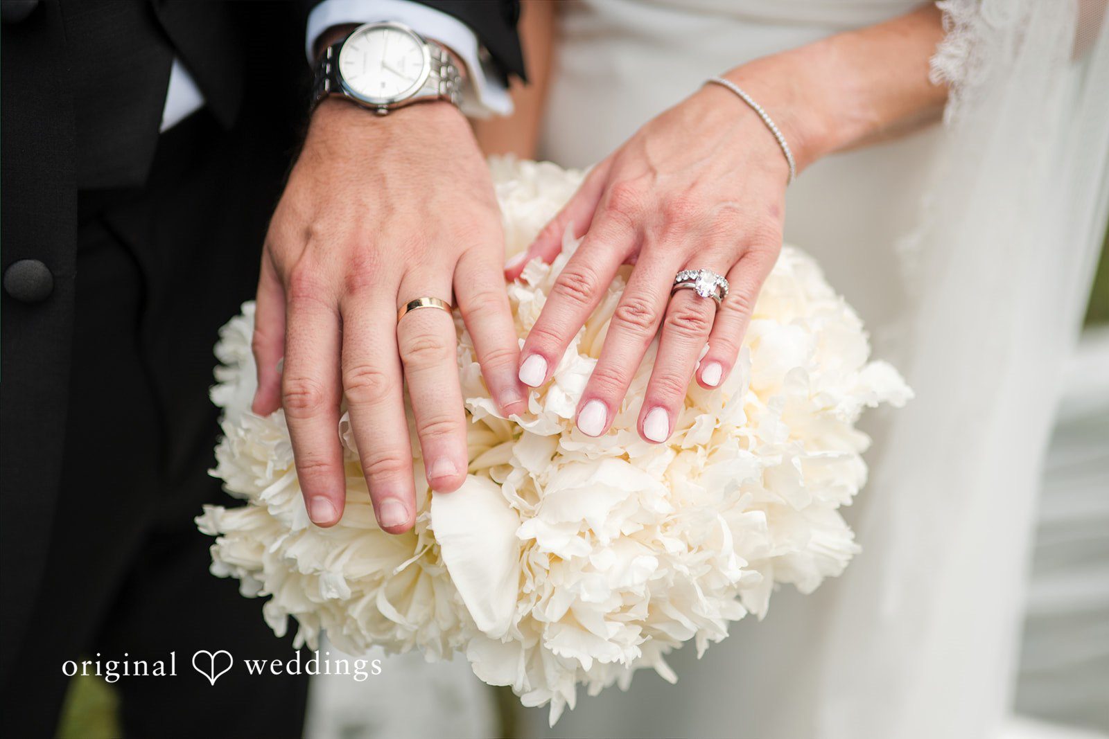 Hands of a groom and bride holding a white rose bouquet.
