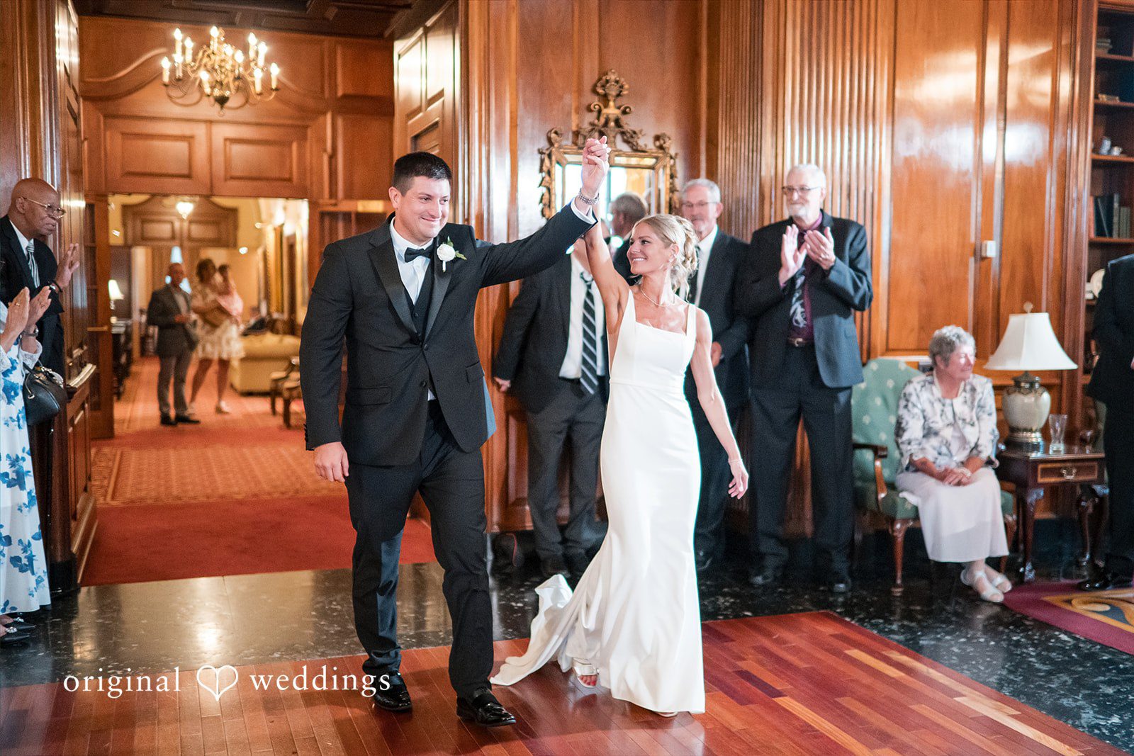 Bride and groom making their grand entrance into a reception hall as guests applaud.