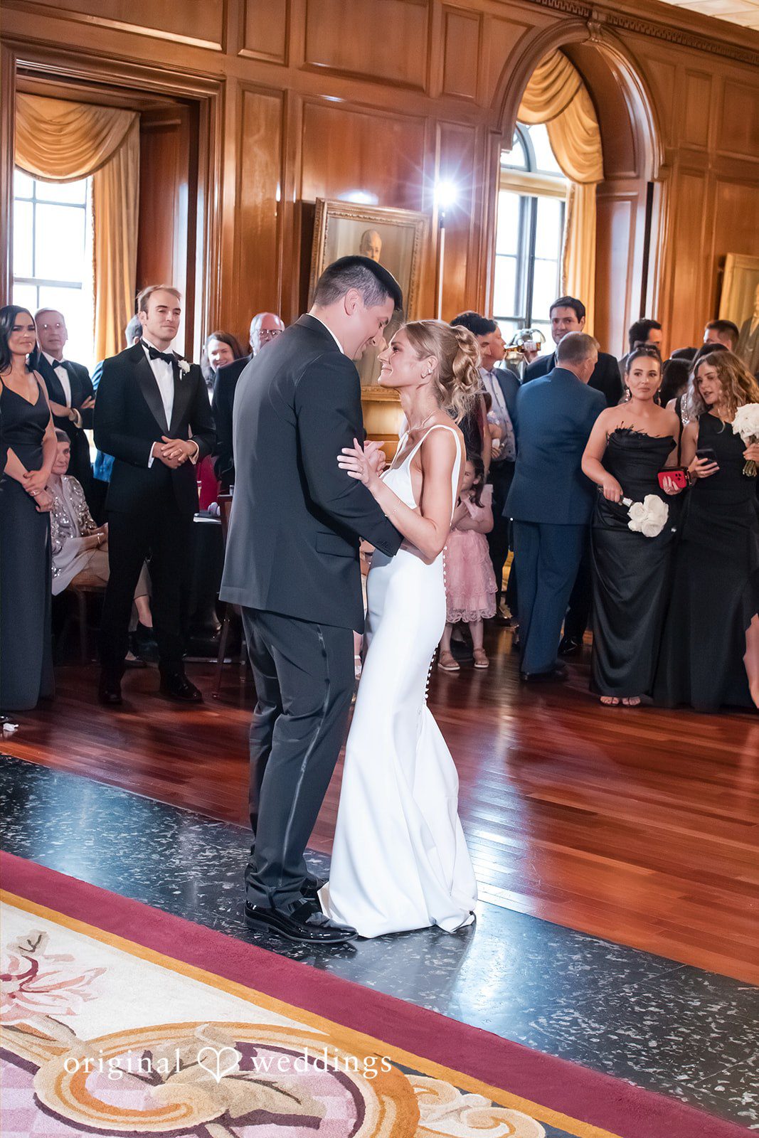 Bride and groom dancing together in the center of a crowded reception dance floor.