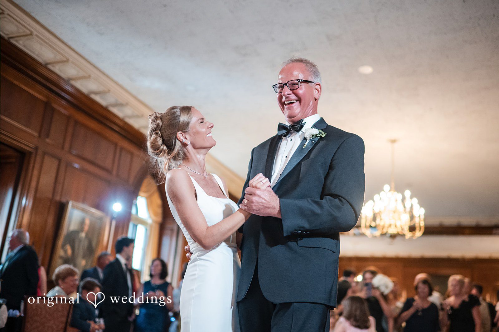 Bride smiling as she dances with an older man in a tuxedo.