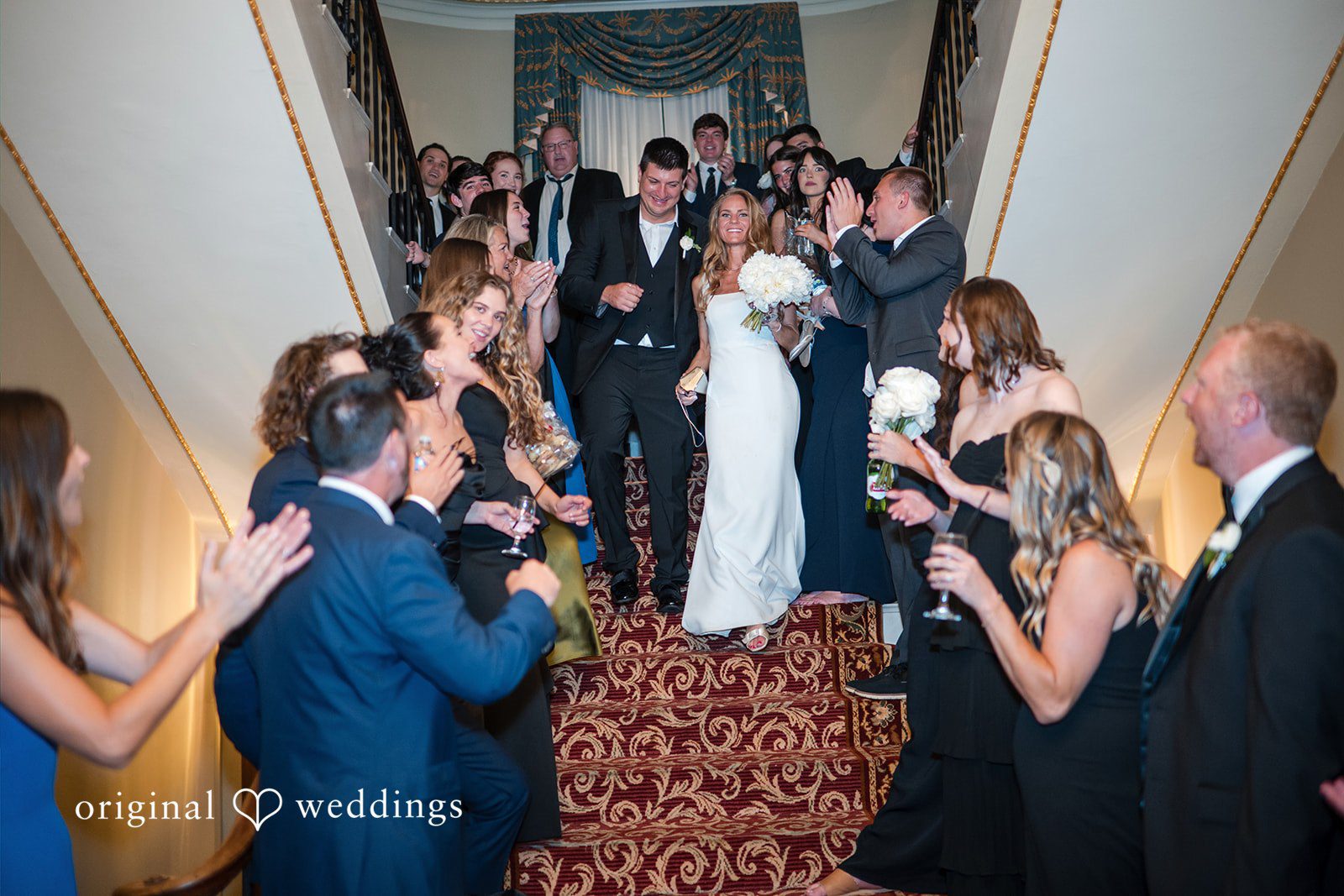 Bride and groom making their grand entrance into a reception hall as guests applaud.