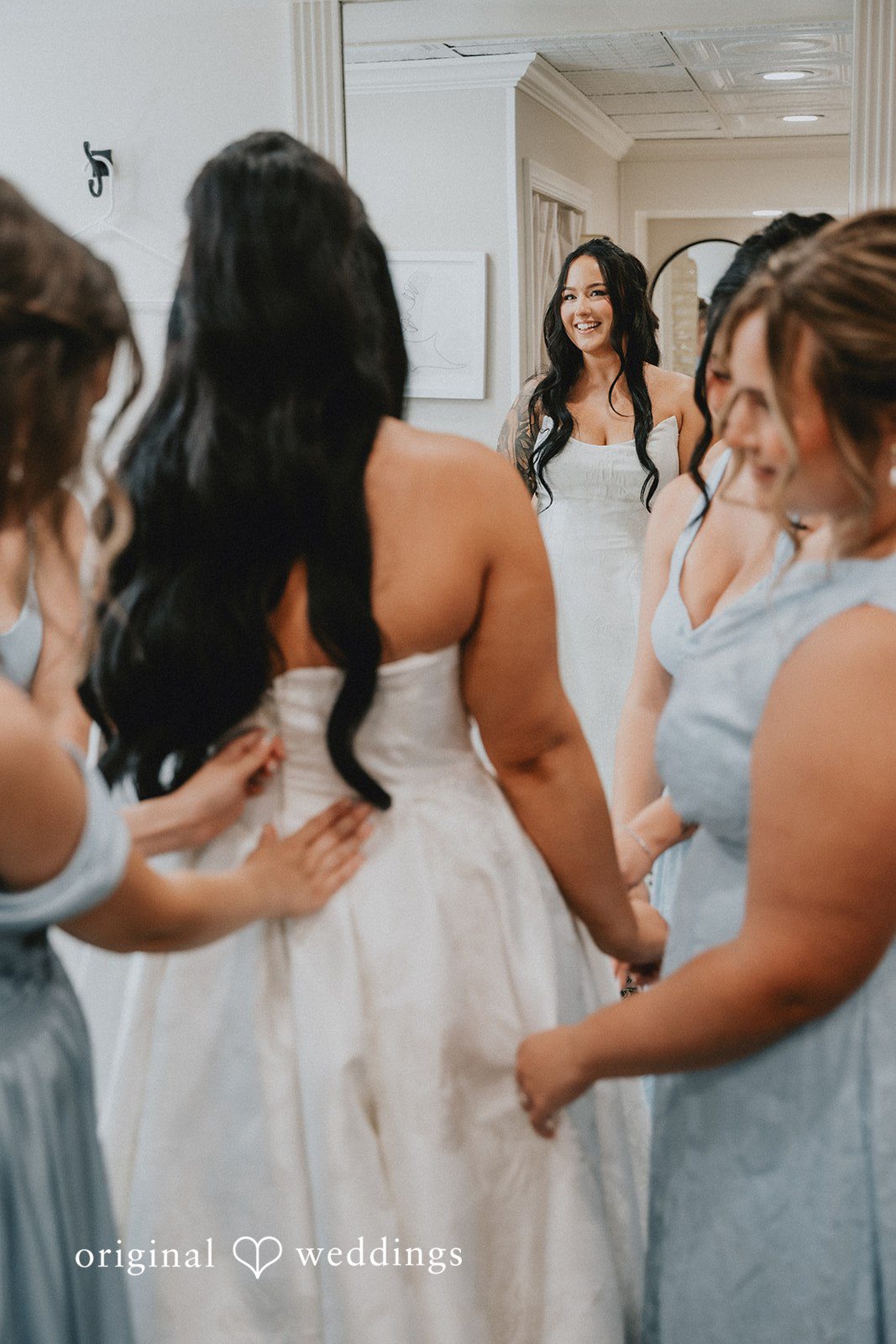 Carly + Dillon A bride having the back of her white wedding dress adjusted by bridesmaids.